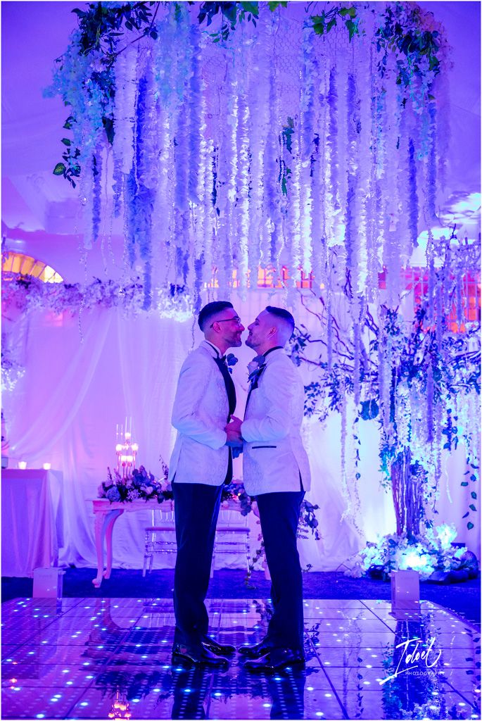A romantic wedding scene with hanging floral decorations and dramatic purple lighting illuminating a dance floor.