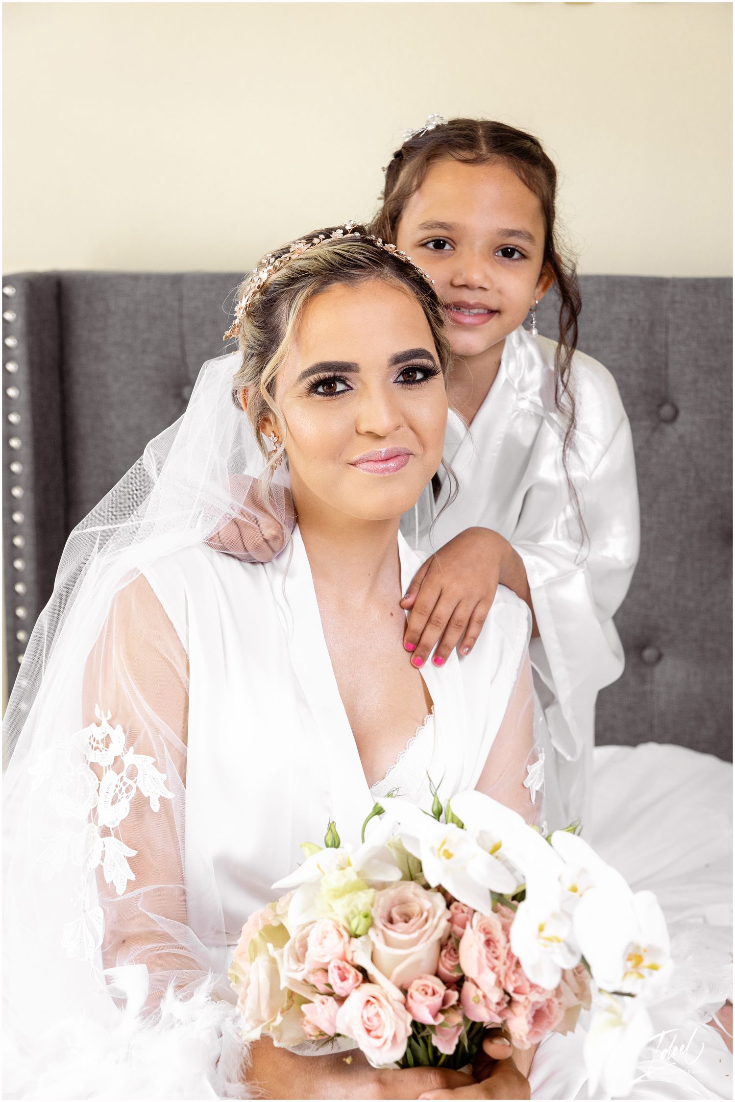 Intimate pre-wedding portrait featuring white robes and elegant pink and white bouquet against gray backdrop.