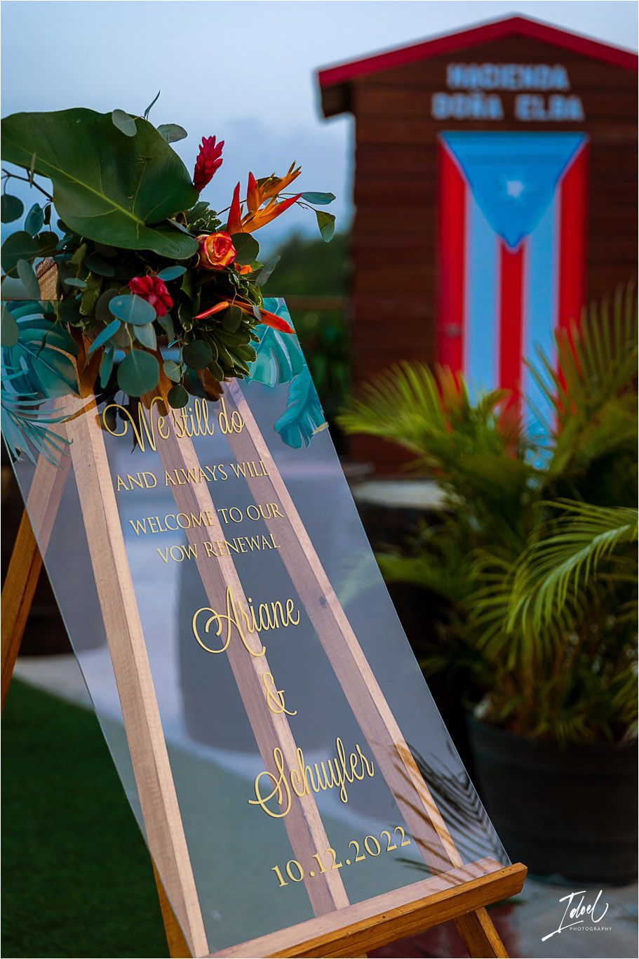 Wedding welcome sign with tropical flowers against a Puerto Rican flag backdrop.