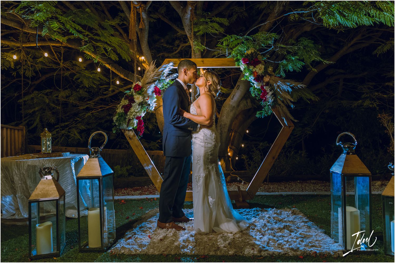 Romantic outdoor wedding ceremony with a lit hexagonal arch and decorative lanterns at dusk.