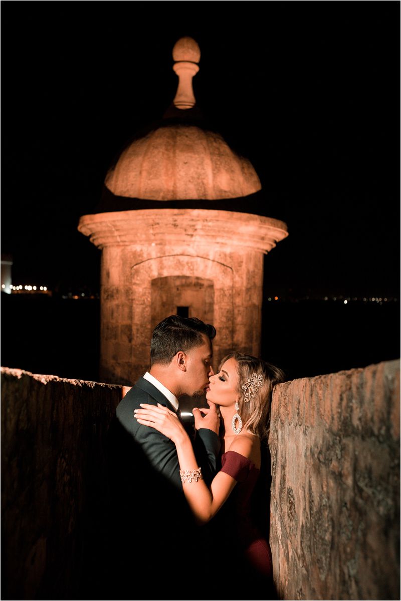 Romantic silhouette of a couple sharing an intimate moment against a stone wall and pillar at night.