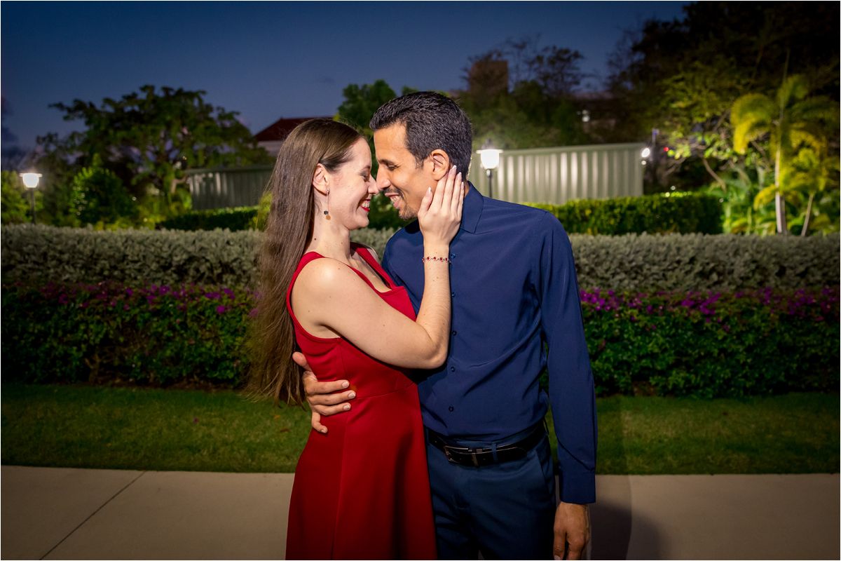 Romantic couple in red dress and blue shirt sharing a tender moment in a garden at night.