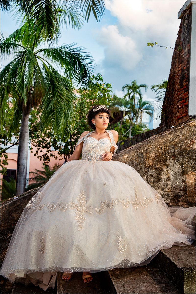 An elegant bridal portrait featuring a ballgown wedding dress surrounded by tropical palm trees and historic architecture.
