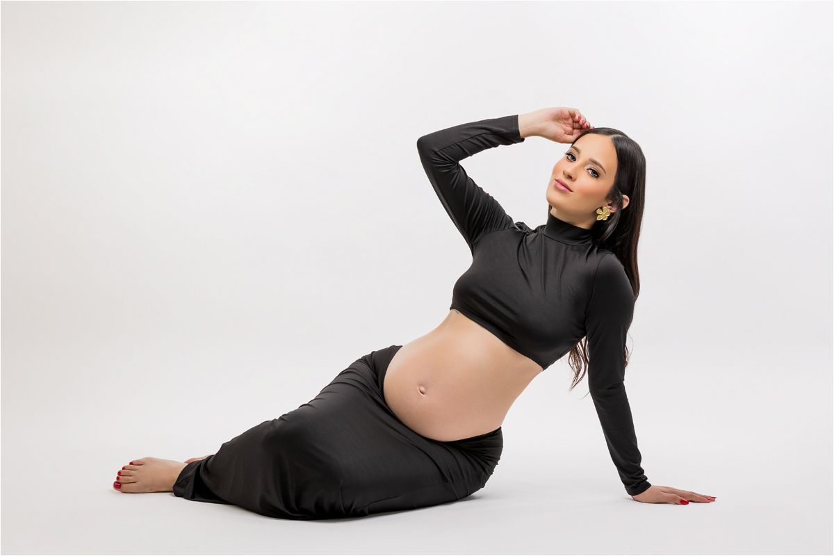 A woman in black athletic wear poses on the floor in a relaxed position against a white background.