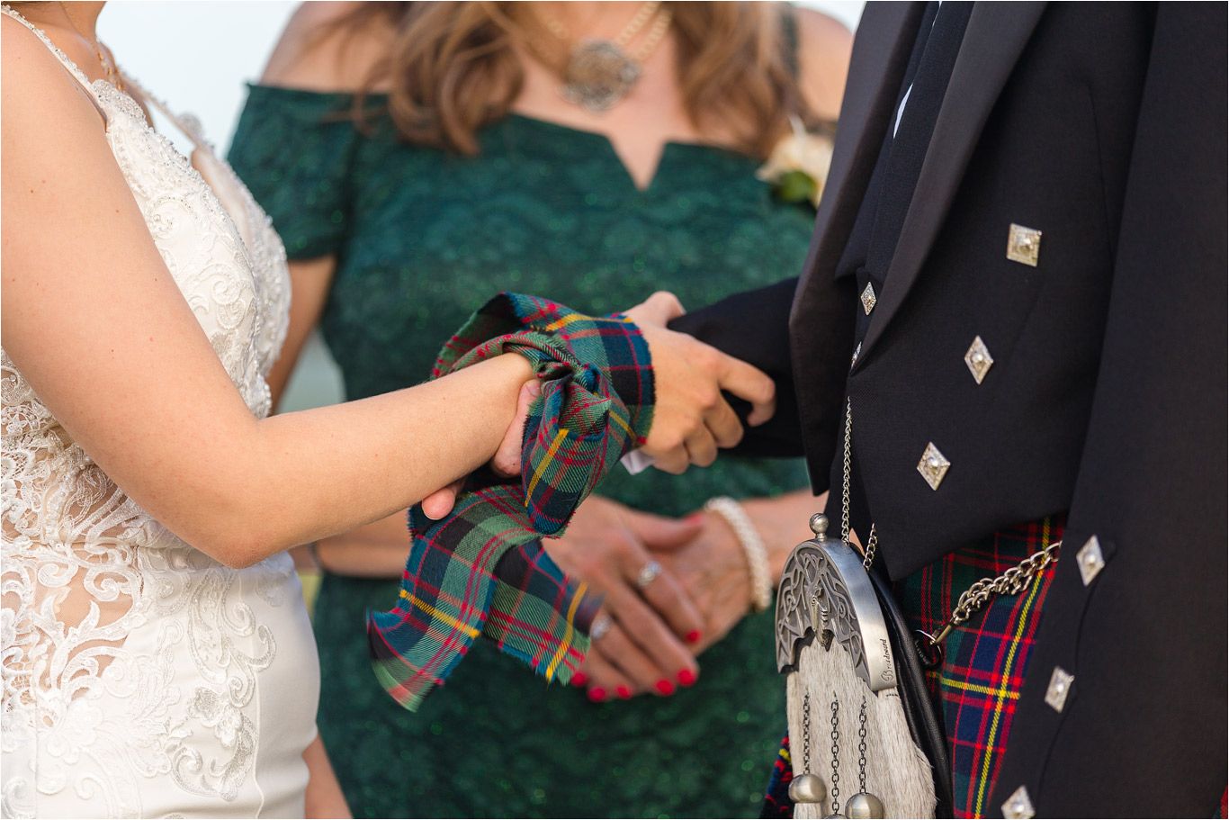 Close-up detail of hands holding a tartan fabric during a traditional Scottish wedding ceremony.