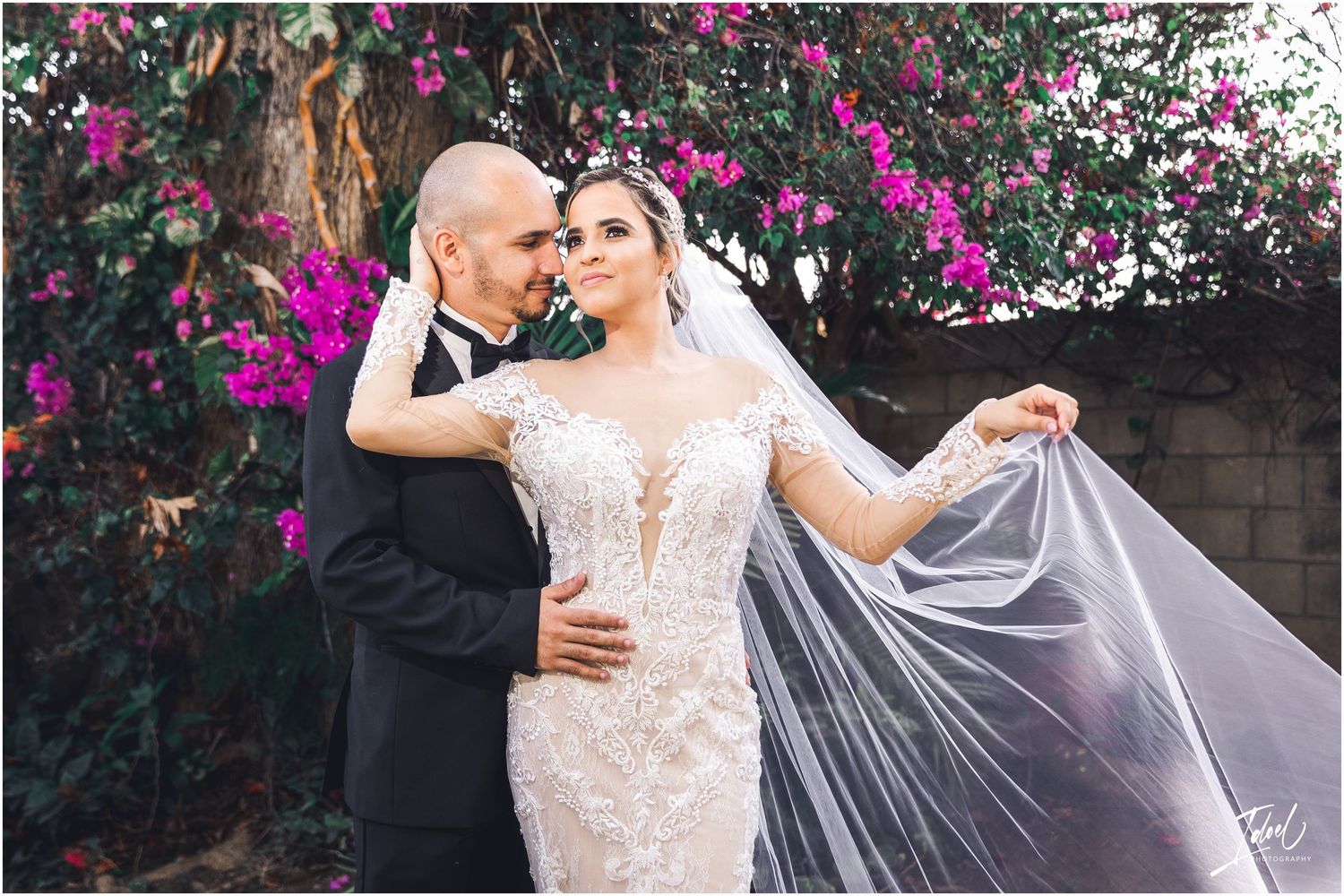 A romantic wedding photo of a couple posing in front of vibrant pink bougainvillea flowers.
