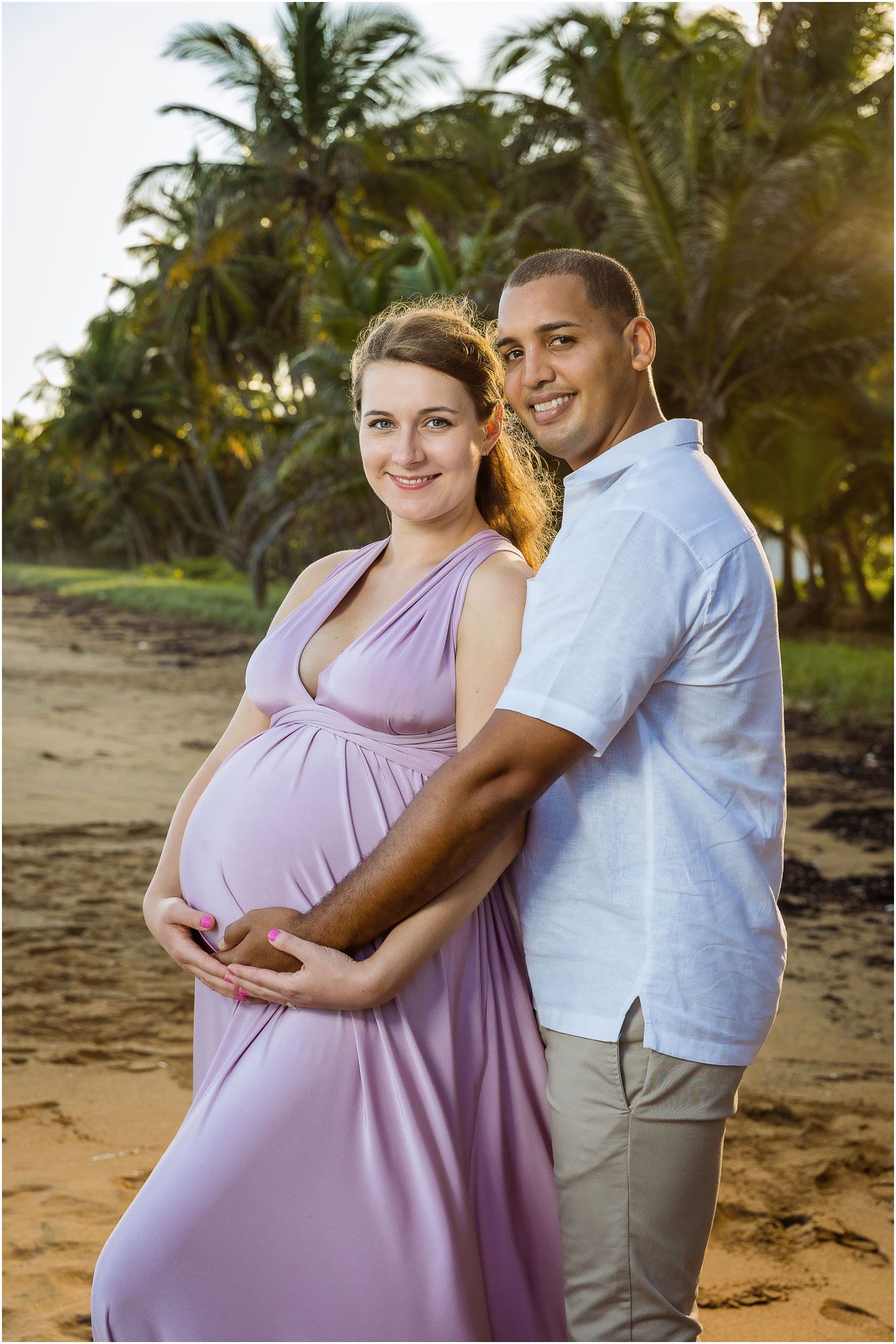 Tropical beach maternity portrait with palm trees and ocean backdrop.