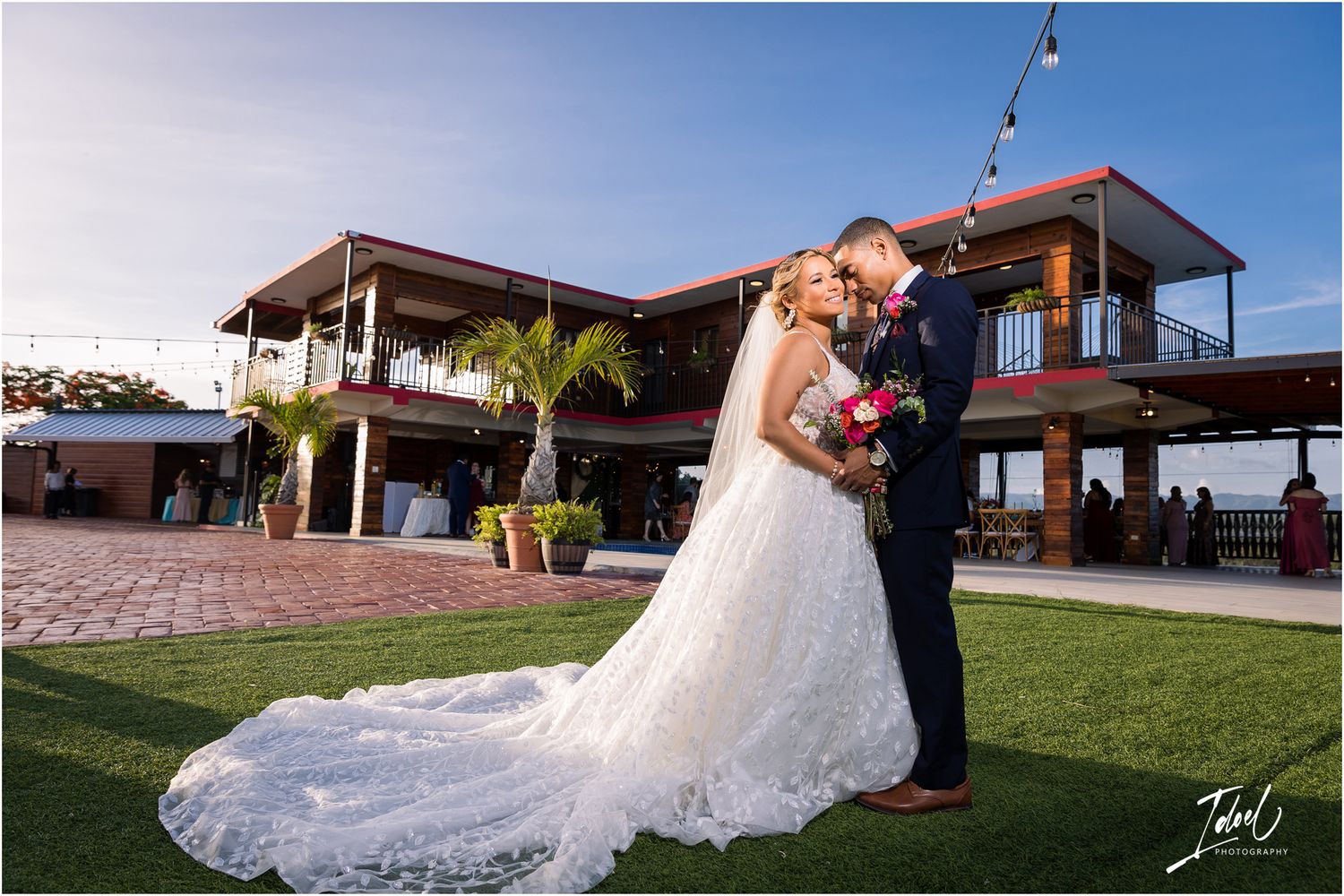 A stunning wedding photo captured at sunset with a two-story modern venue as the backdrop.