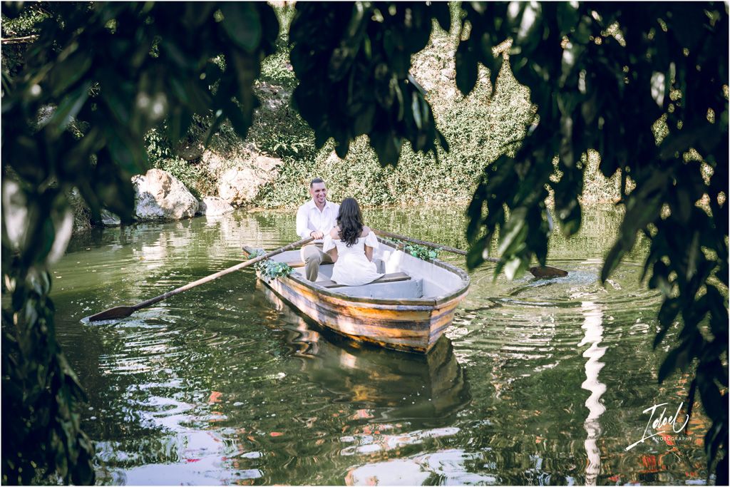 Someone rows a small boat peacefully through tranquil waters surrounded by overhanging tree branches and foliage.