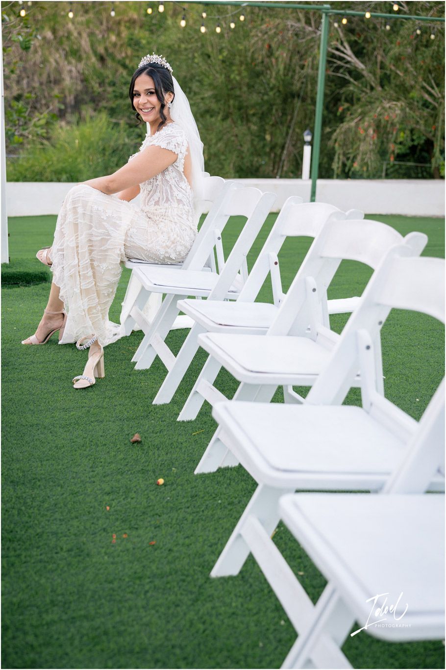 Elegant white wedding setup with folding chairs arranged on green turf and bridal attire being showcased in outdoor setting.