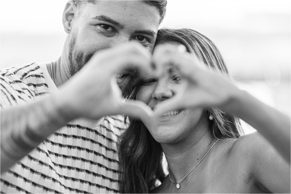 A couple forms a heart shape with their hands while sharing an intimate black and white moment together.