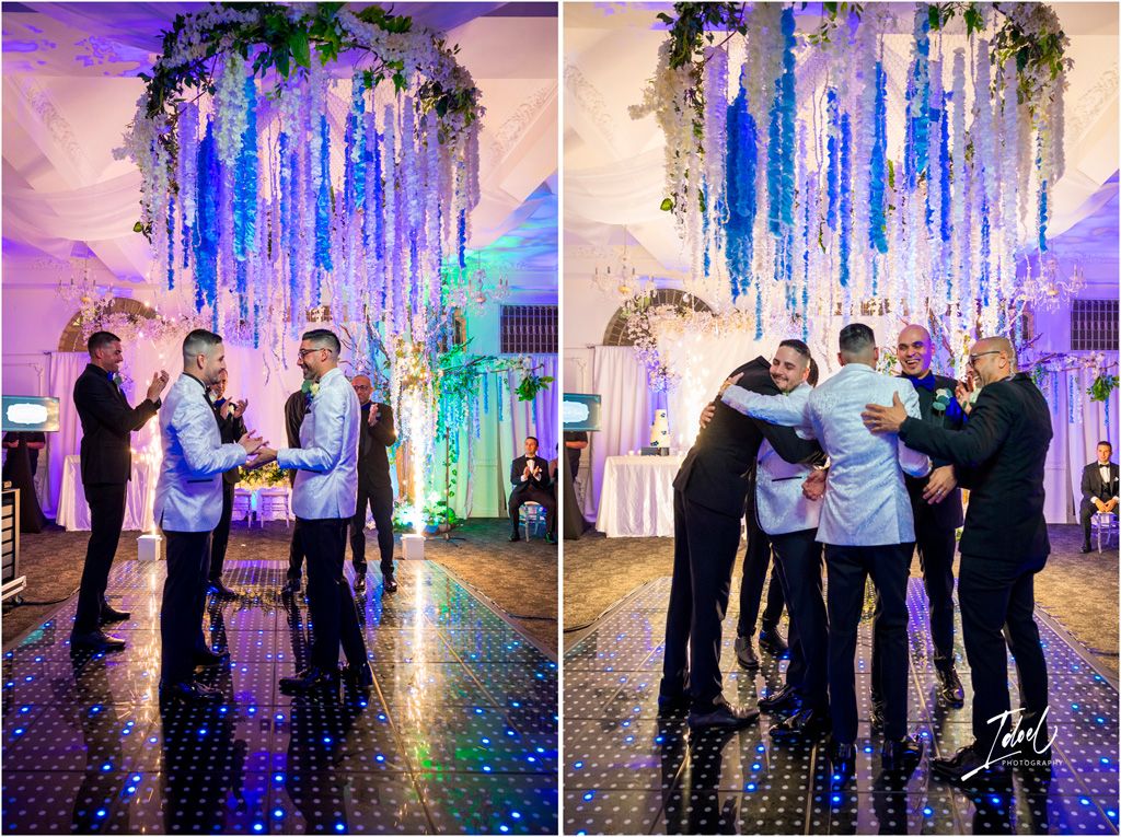 A celebration in a wedding venue with elegant blue hanging florals and purple lighting creating a magical atmosphere.