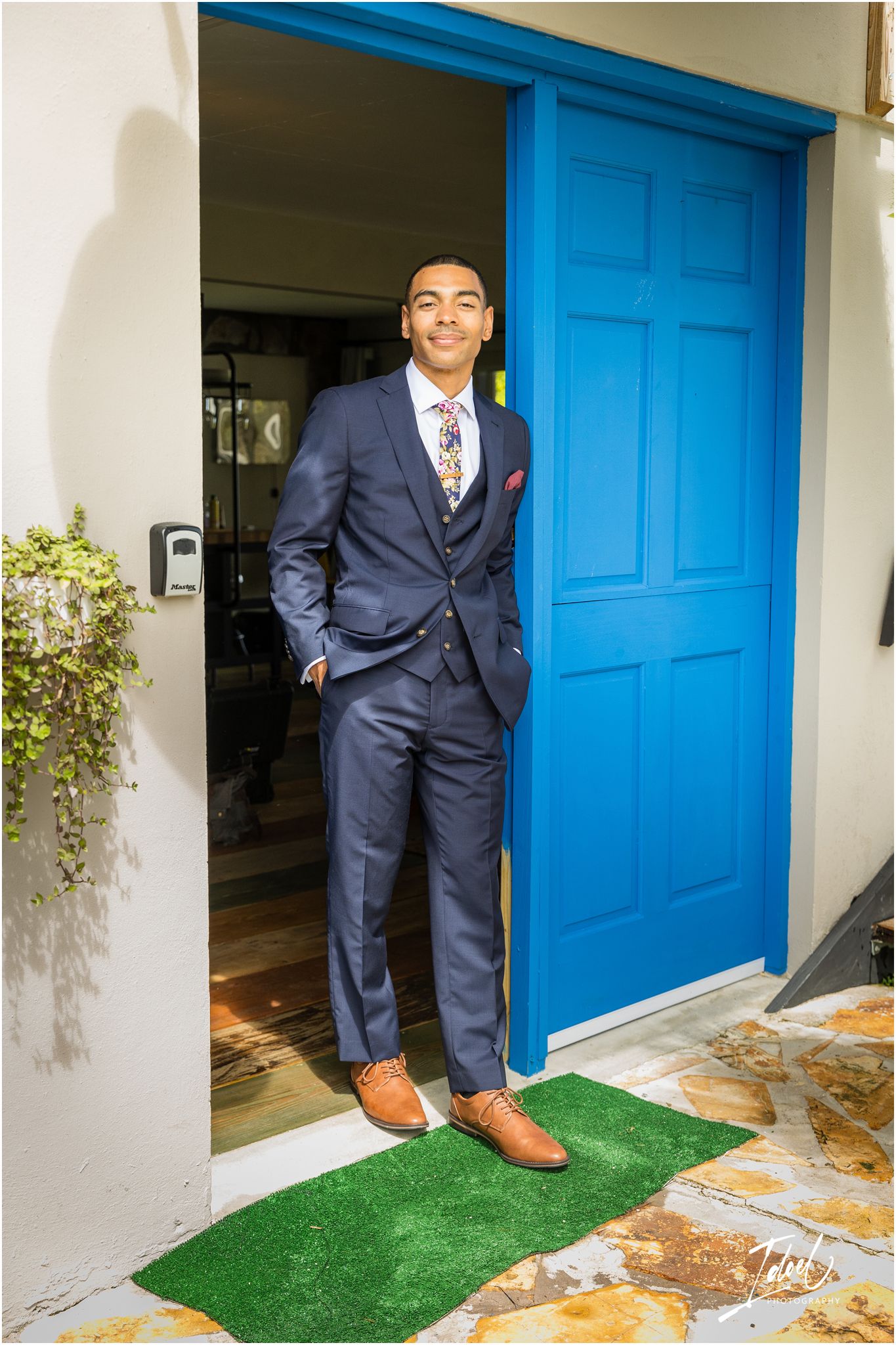 Well-dressed person in navy suit stands confidently by bright blue door.