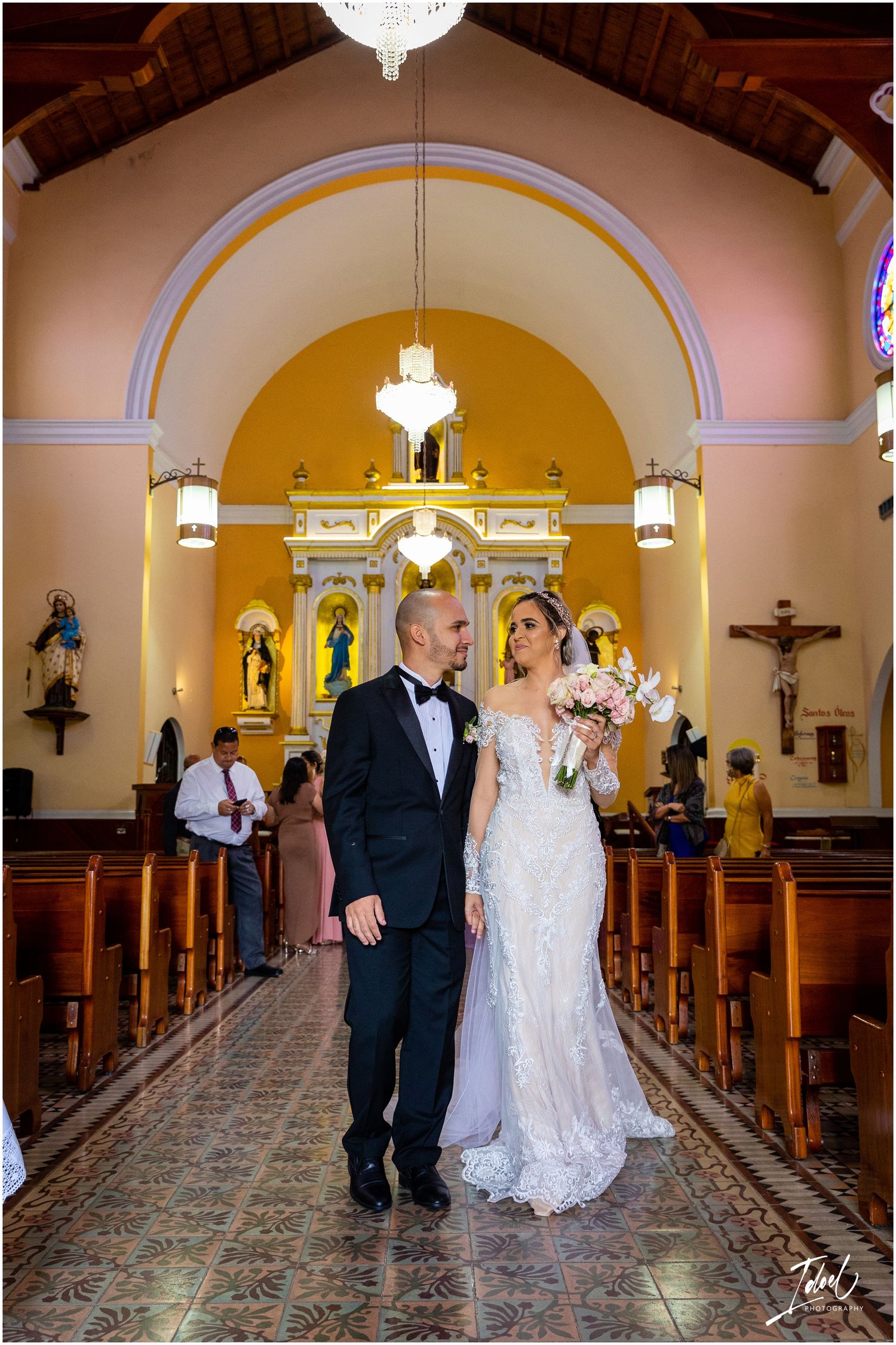 Newlyweds pose in church aisle under arched ceiling with ornate altar in background.
