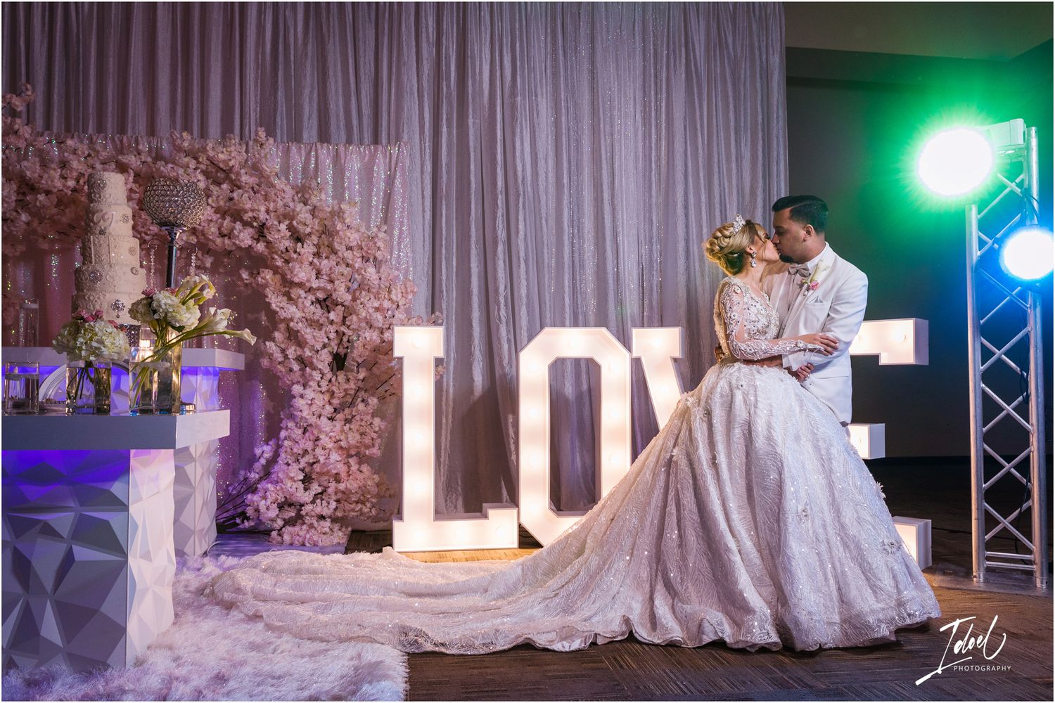 A romantic wedding scene with illuminated LOVE letters and blush floral arrangements.
