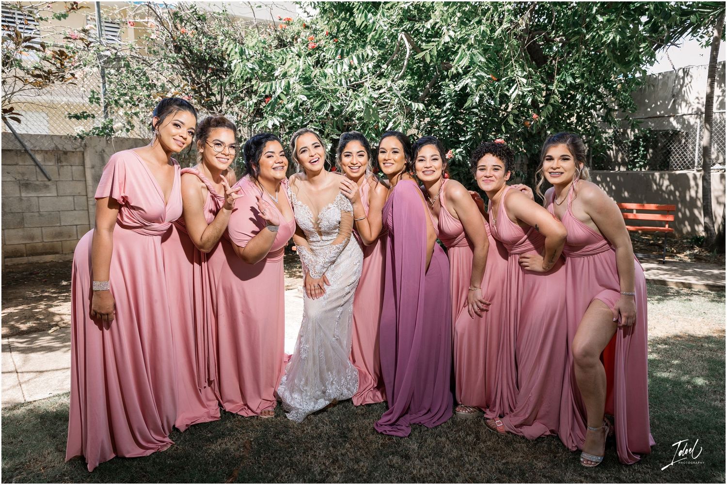 Bridal party in flowing pink and purple dresses poses together in a garden setting.