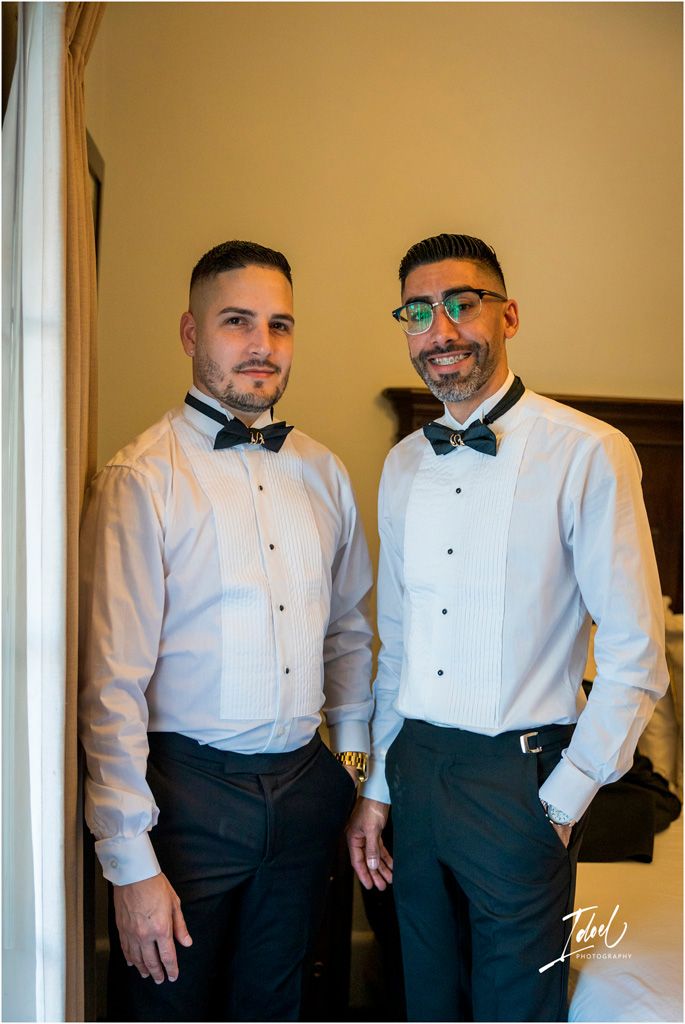 Two men in white dress shirts and bow ties pose together in formal attire at a special event.