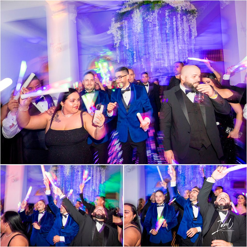 Wedding party celebrates on dance floor with glow sticks under blue and purple lighting and crystal chandelier decorations.