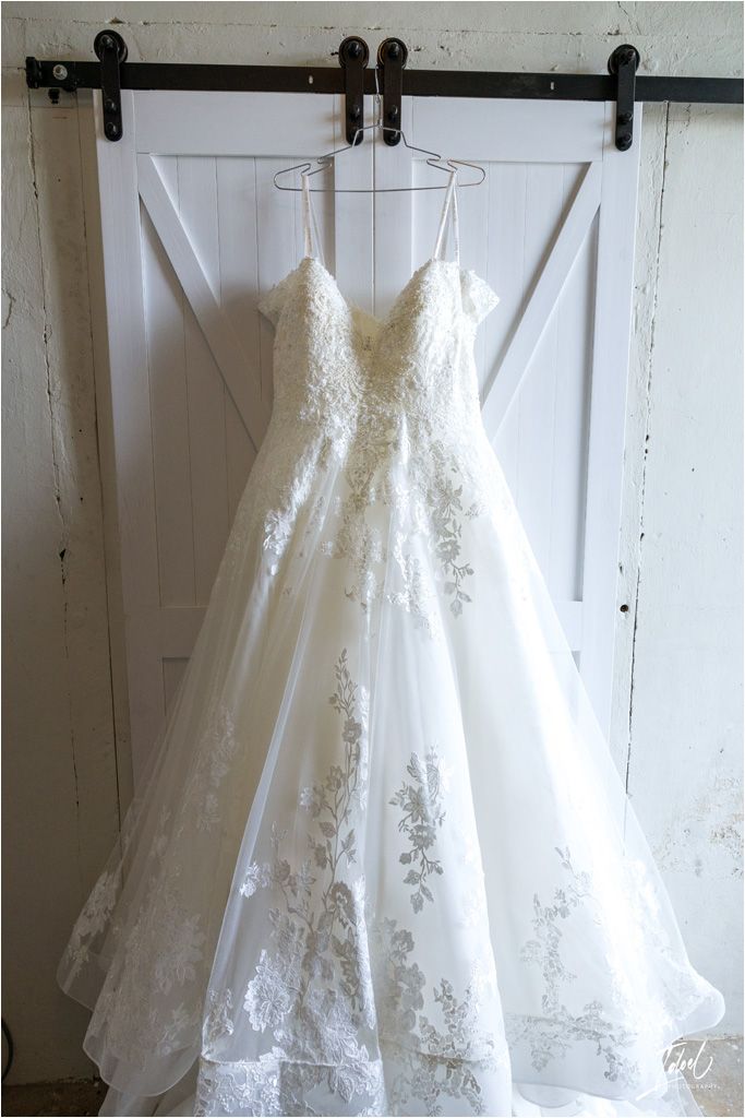 An elegant white lace wedding dress hangs on a barn door with black hardware.
