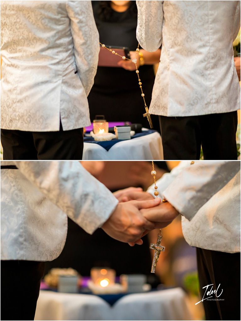 Two people in white jackets hold a rosary together during a ceremony with candles in the background.