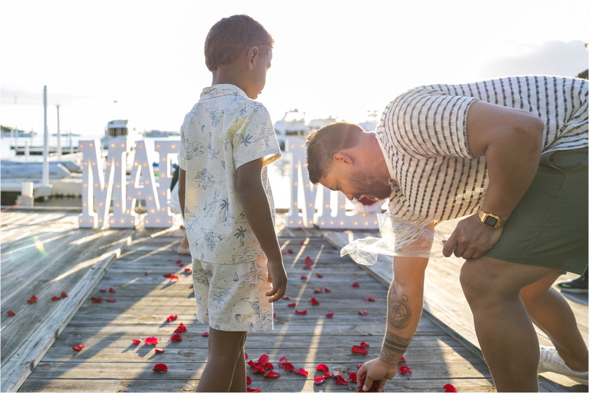Two people play a game with red and white pieces on a sunny pier by the water.