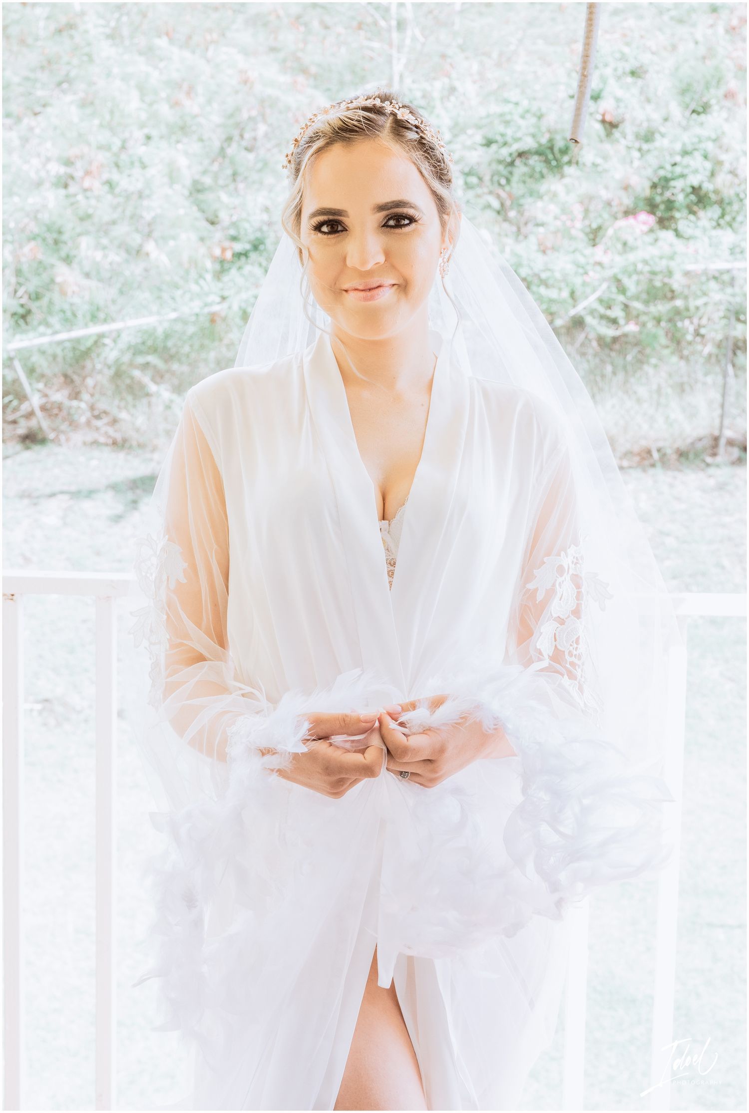 Ethereal bridal portrait with flowing veil against floral background in natural light.