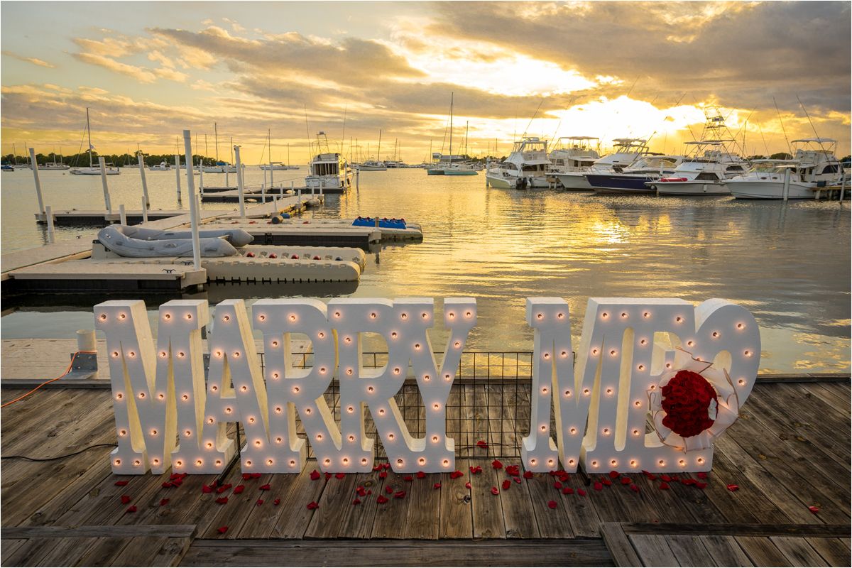 Crystal-like letters spelling out 'Mr & Mrs' on a wooden dock overlooking boats in a harbor at golden sunset.