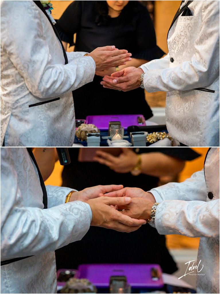 Two people in light brocade jackets exchange rings during a wedding ceremony with purple decor in the background.