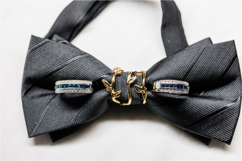 Wedding rings placed on black silk bow tie with gold accent in elegant detail shot.