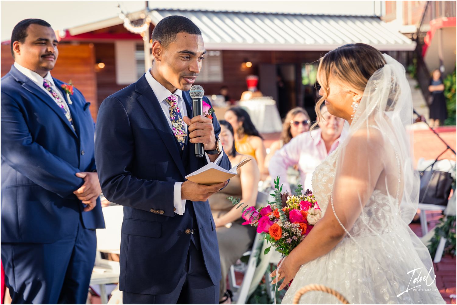 Couple exchanging vows during outdoor wedding ceremony with pink floral details.