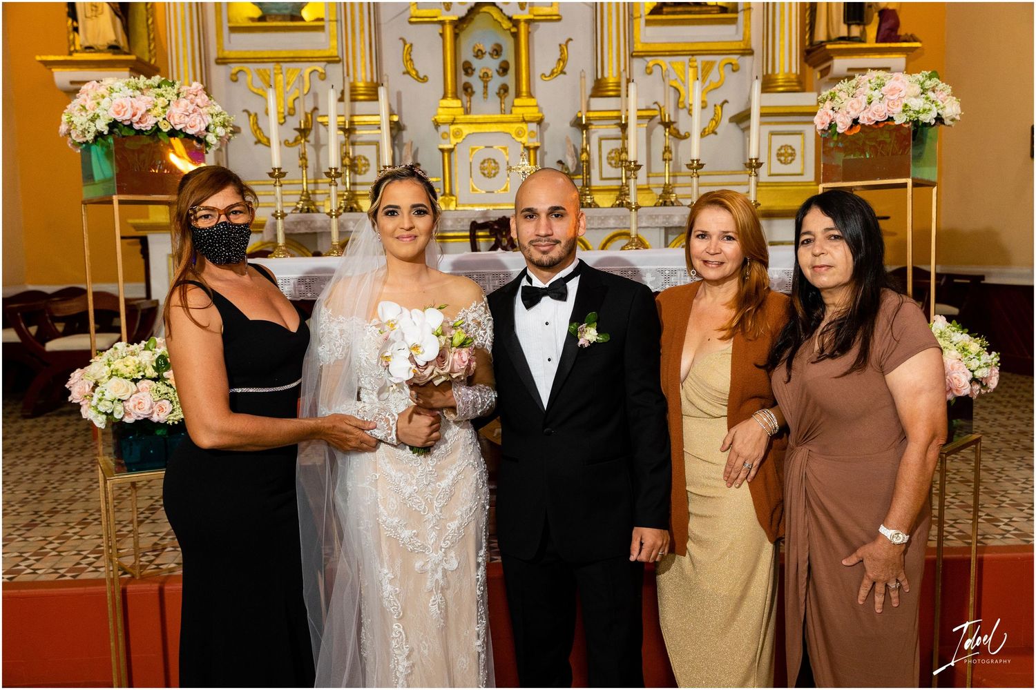 Small wedding group poses in formal attire against golden church altar backdrop.