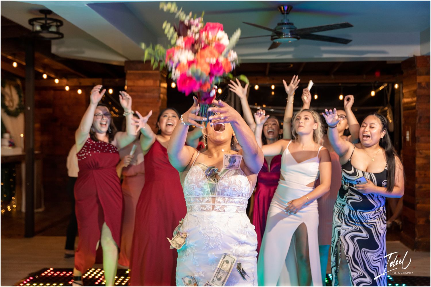 A joyful wedding celebration with a bouquet toss moment showing excitement and colorful dresses on a dance floor.