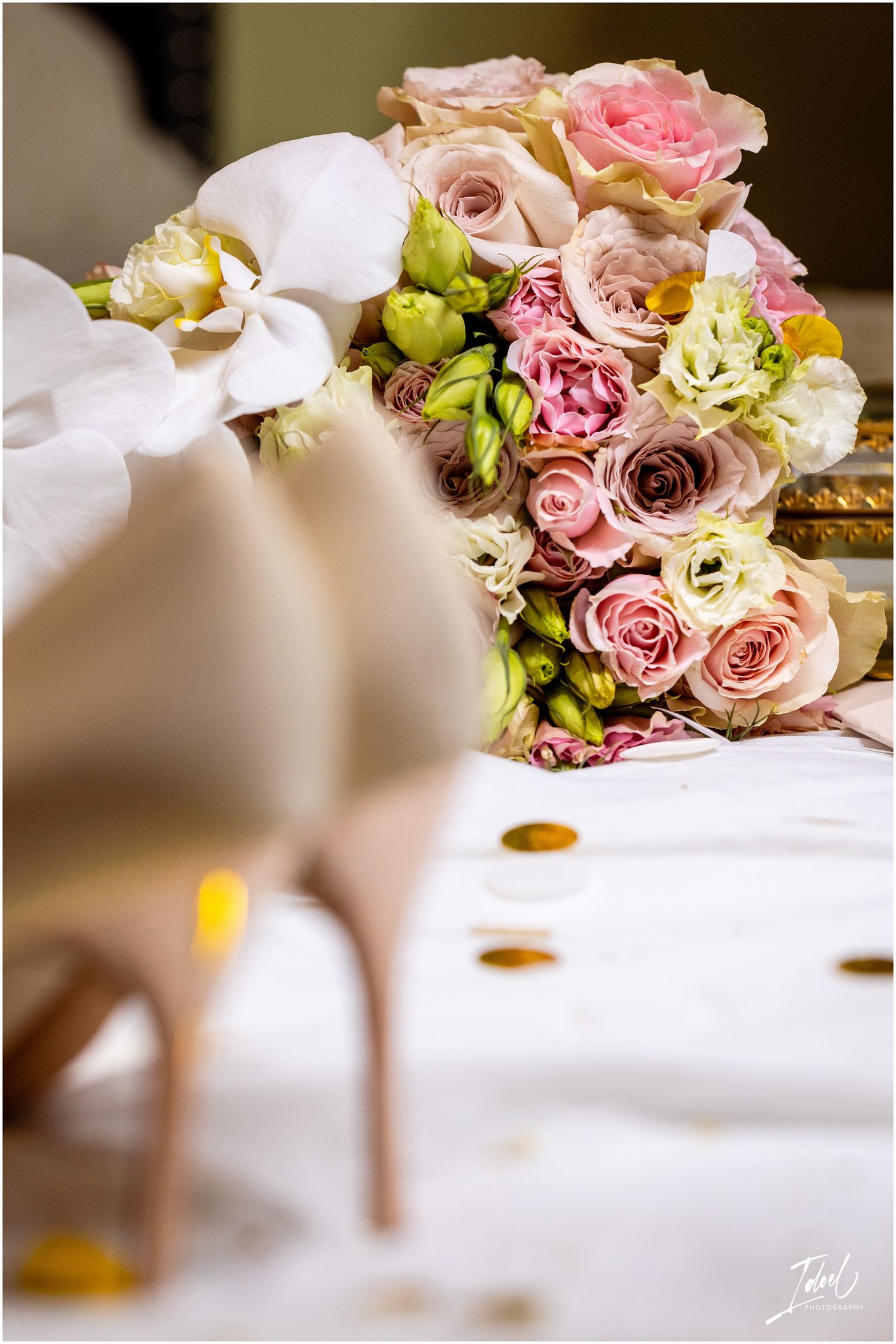 A romantic bridal bouquet with pink roses, white orchids and green accents on a white surface.
