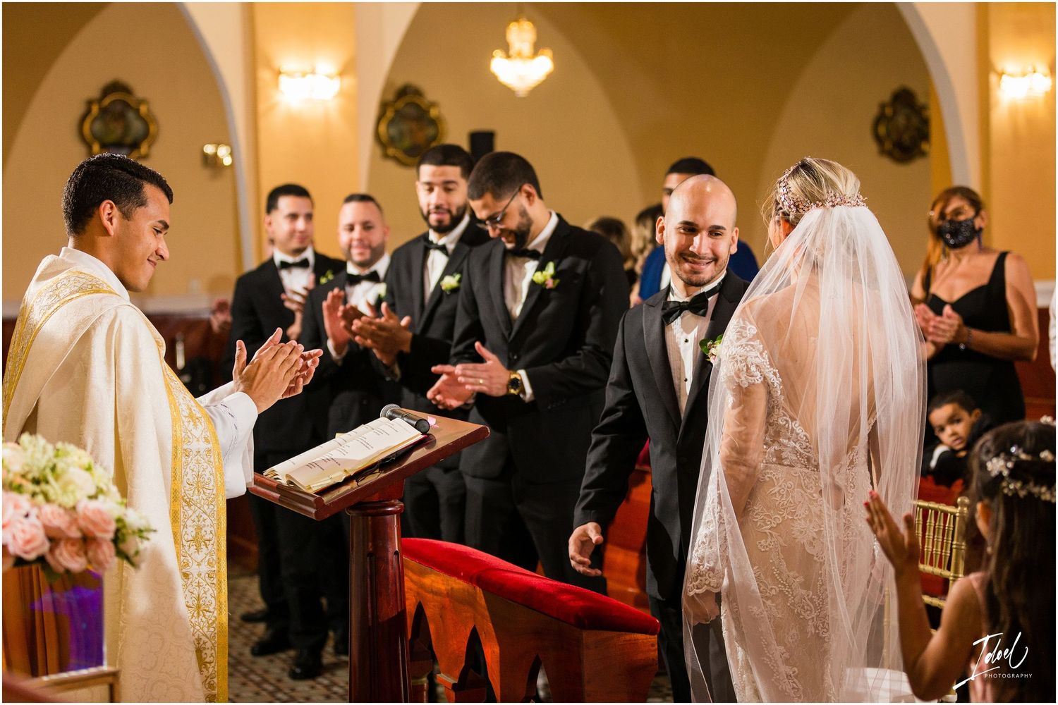 Wedding ceremony in progress with priest and attendants in traditional church setting.