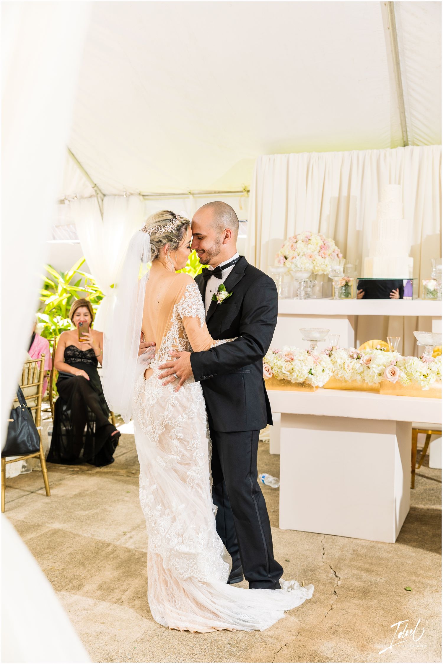 Couple shares first dance in elegant outdoor tent setting with white decor and floral arrangements.