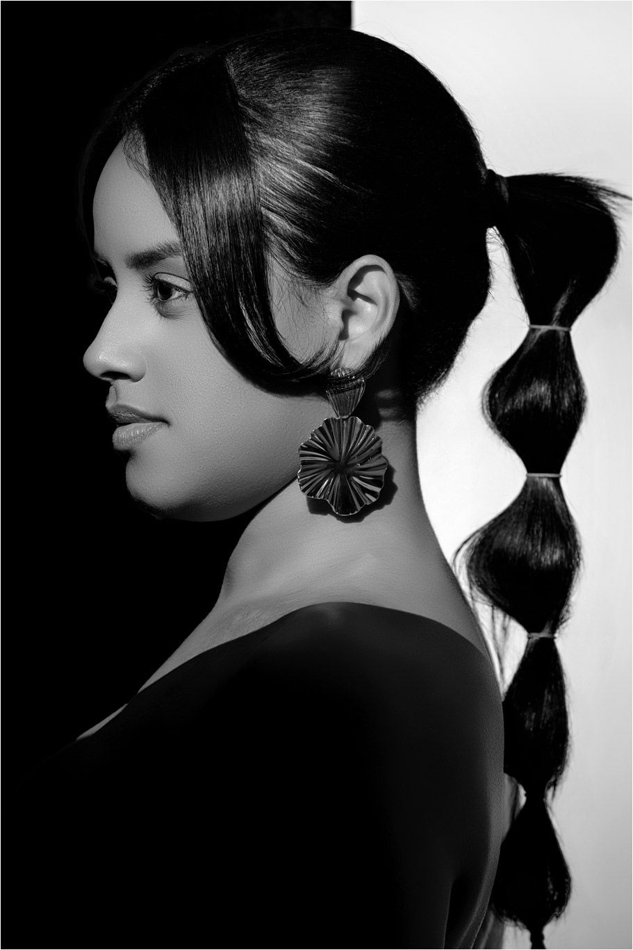 Black and white profile portrait of woman with elegant bubble ponytail and floral earring.