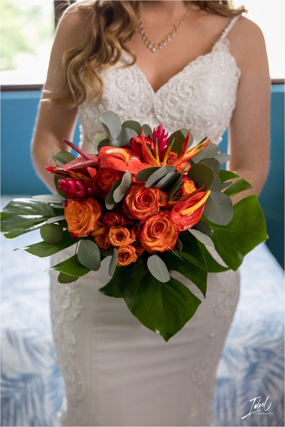 Detail shot of bridal bouquet with orange roses and red lilies against white lace dress.
