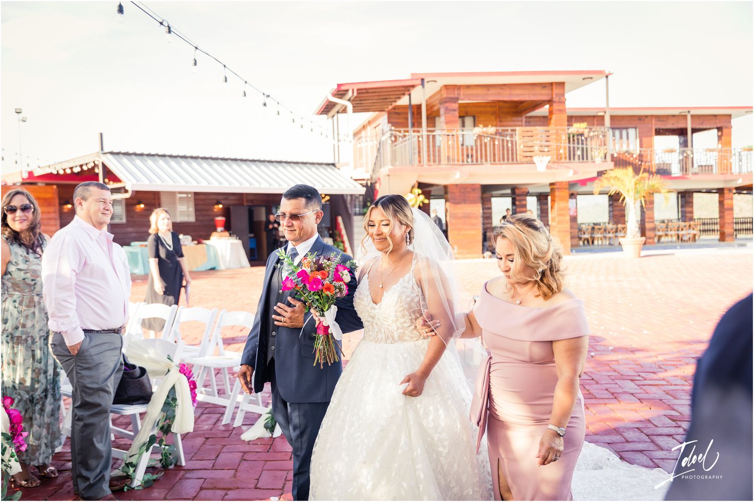 Wedding celebration on a brick patio with string lights and a coral-colored building in the background.