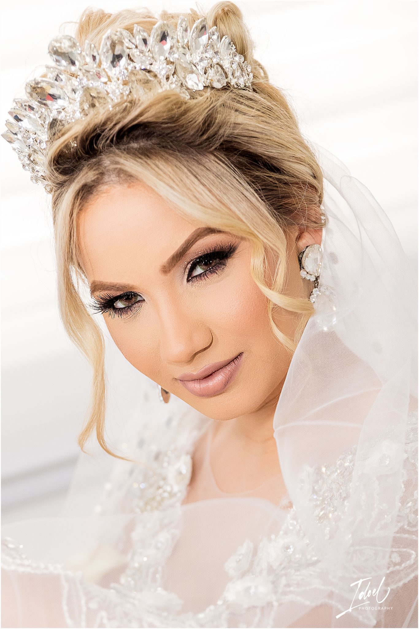 Close-up portrait of bride wearing ornate crystal crown, veil and delicate makeup for wedding day.