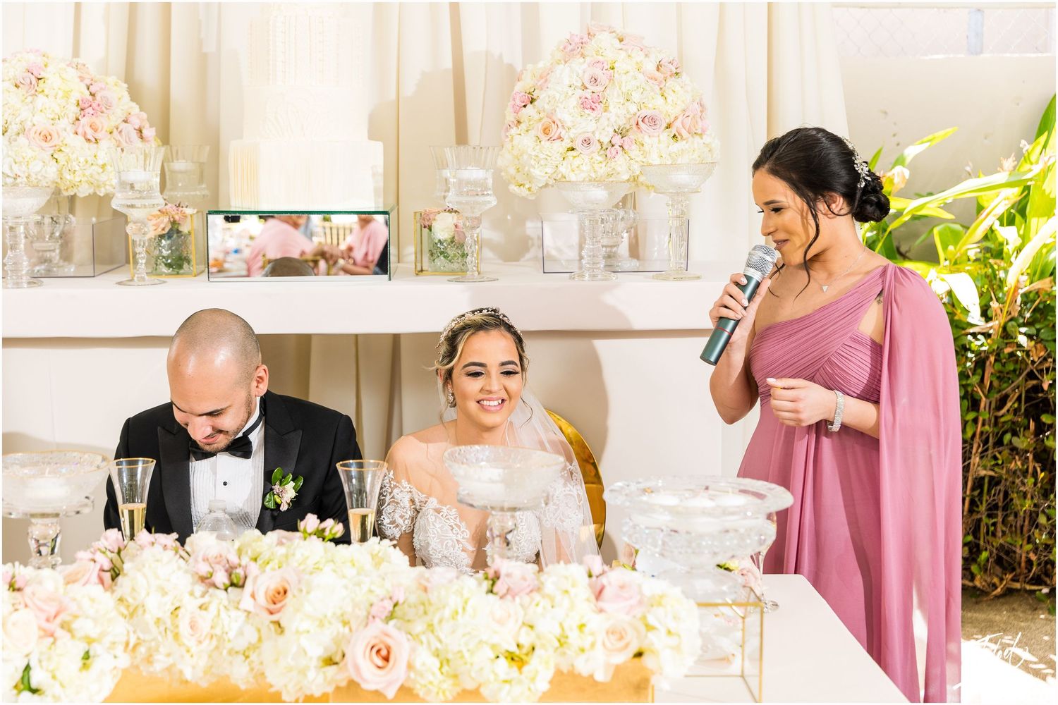 A wedding reception scene with elegant table settings and floral arrangements as guests give speeches.