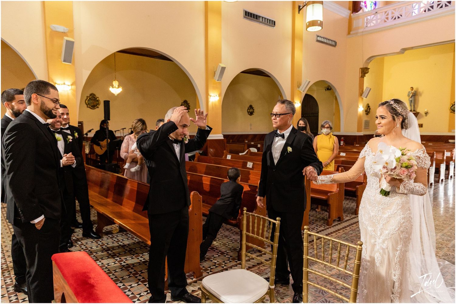 Wedding guests and bridal party celebrate in the aisle of a church with yellow walls and arched architecture.