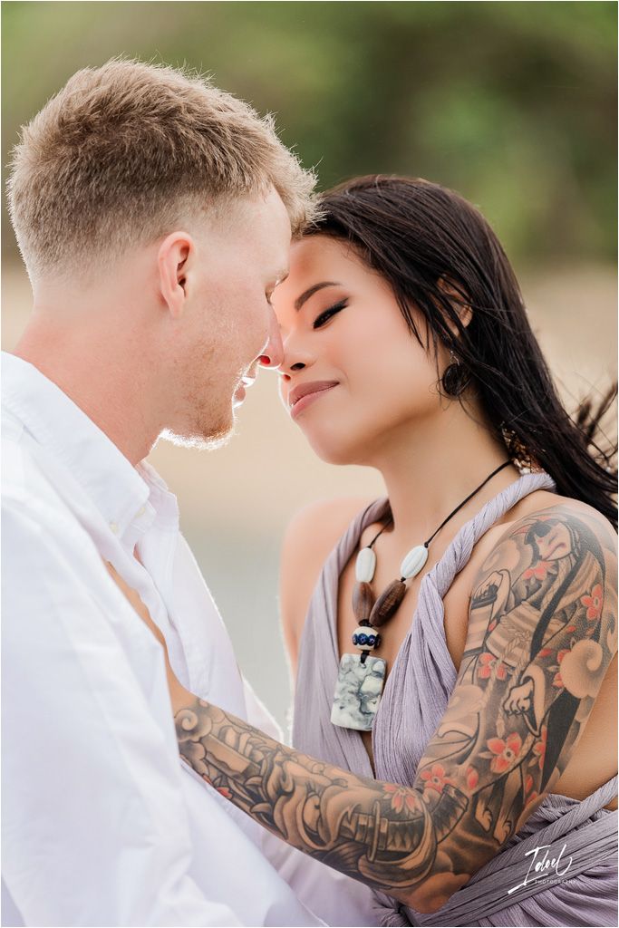 Intimate couple sharing tender moment outdoors with visible tattoo art.