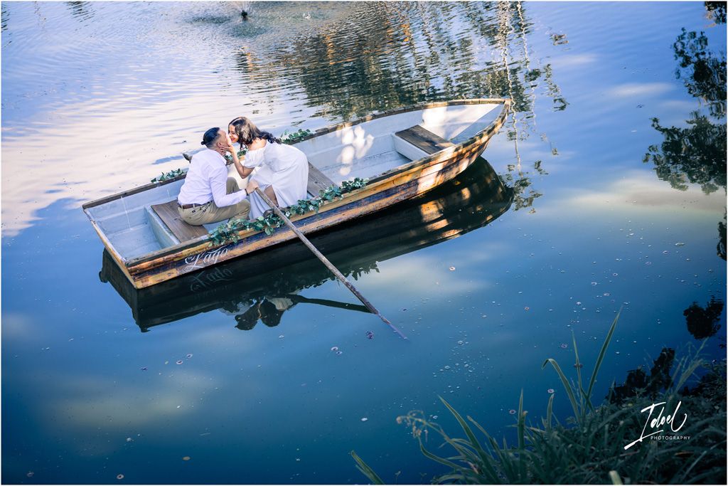A couple sitting in a wooden rowboat on calm reflective water during a romantic sunset moment.