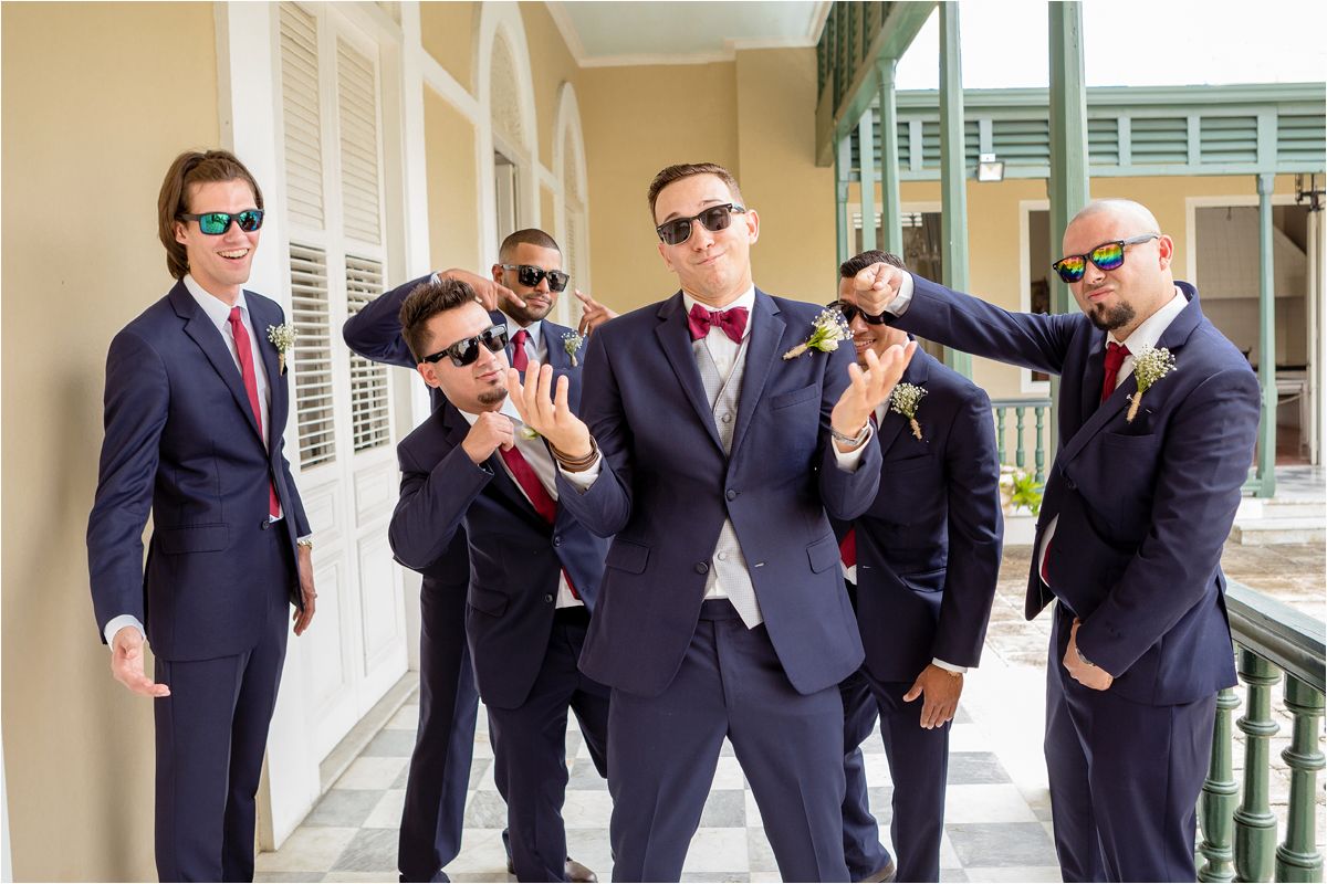 A group of groomsmen in navy suits and sunglasses pose playfully in a sequence of candid shots at a wedding venue.