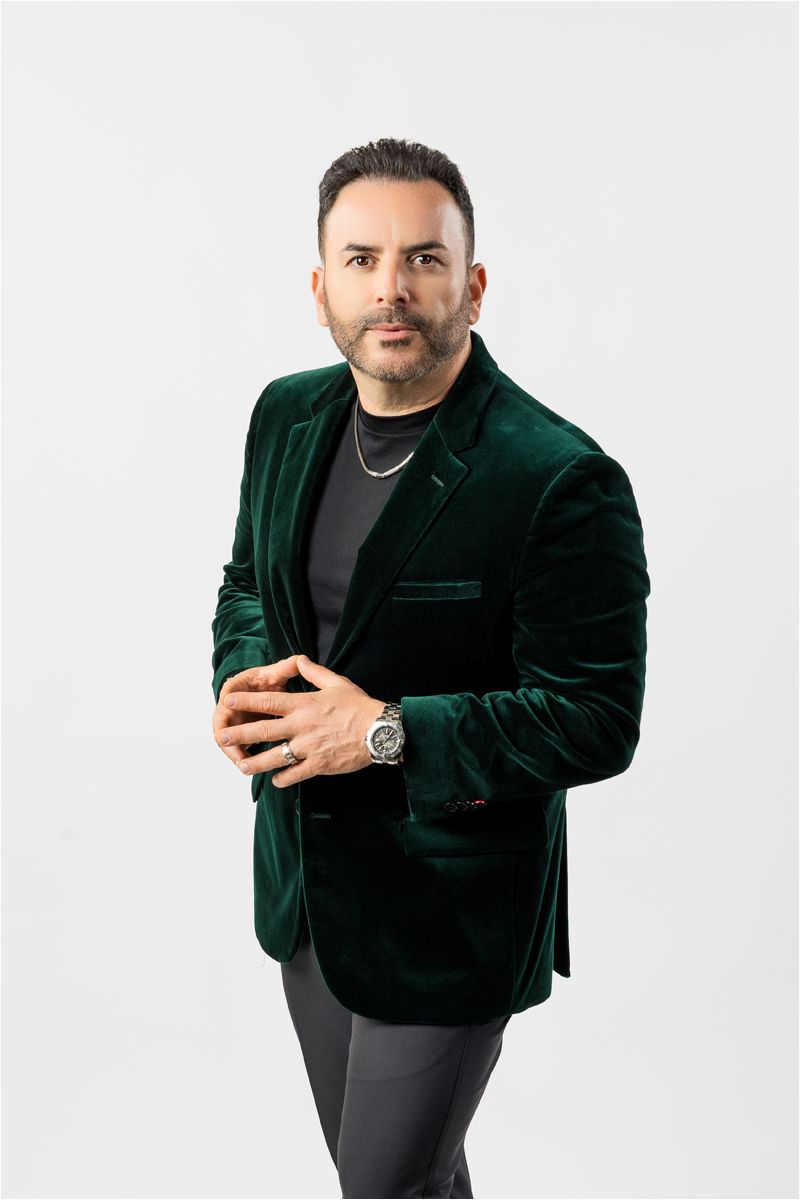 Professional portrait of a person in an emerald green velvet blazer and black shirt against a white backdrop.