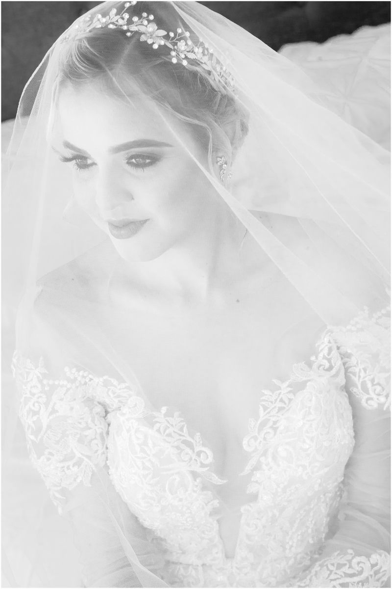 Black and white portrait of a bride wearing a delicate lace wedding gown and veil with floral details.