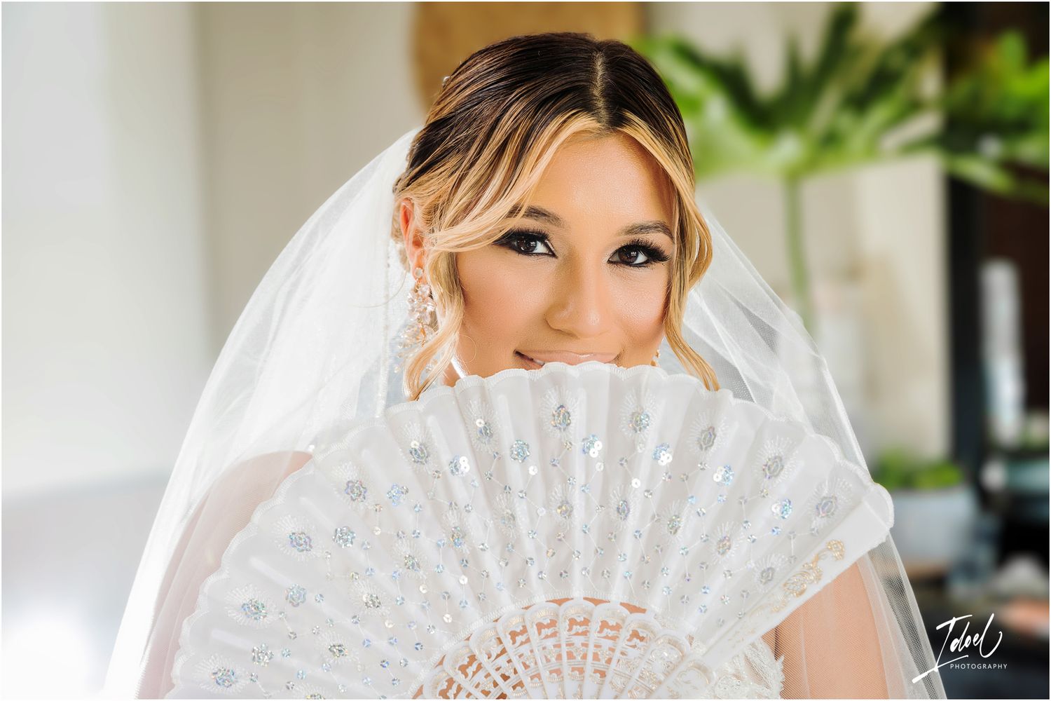 Bride holding decorative white lace fan poses with elegant bridal makeup and veil.