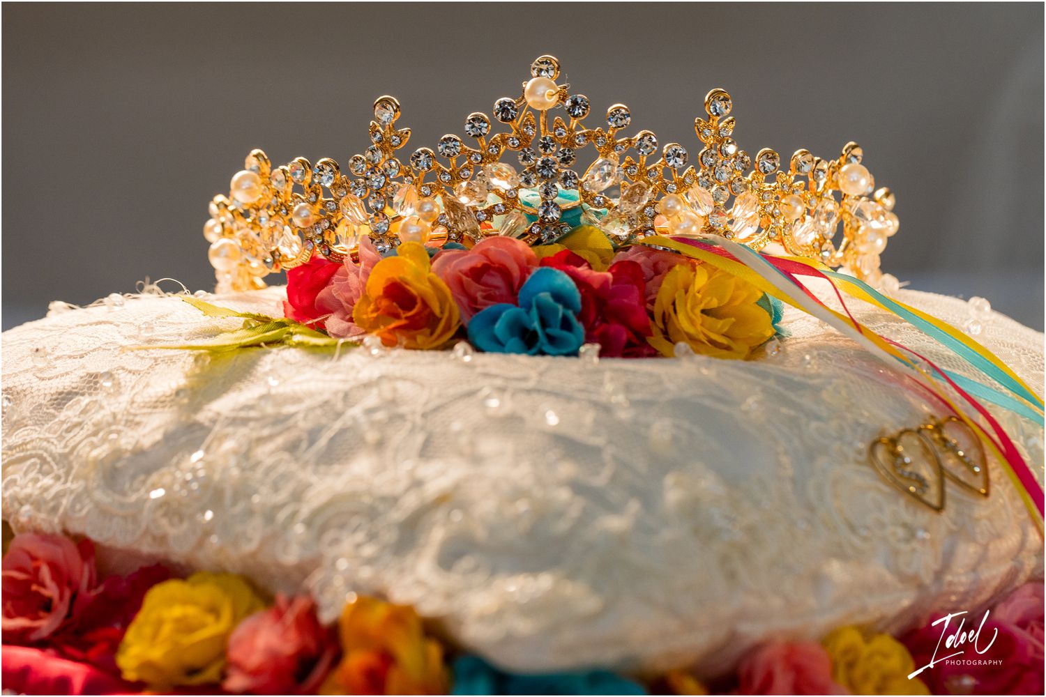 An ornate golden crown sits atop colorful roses on a white textured surface.