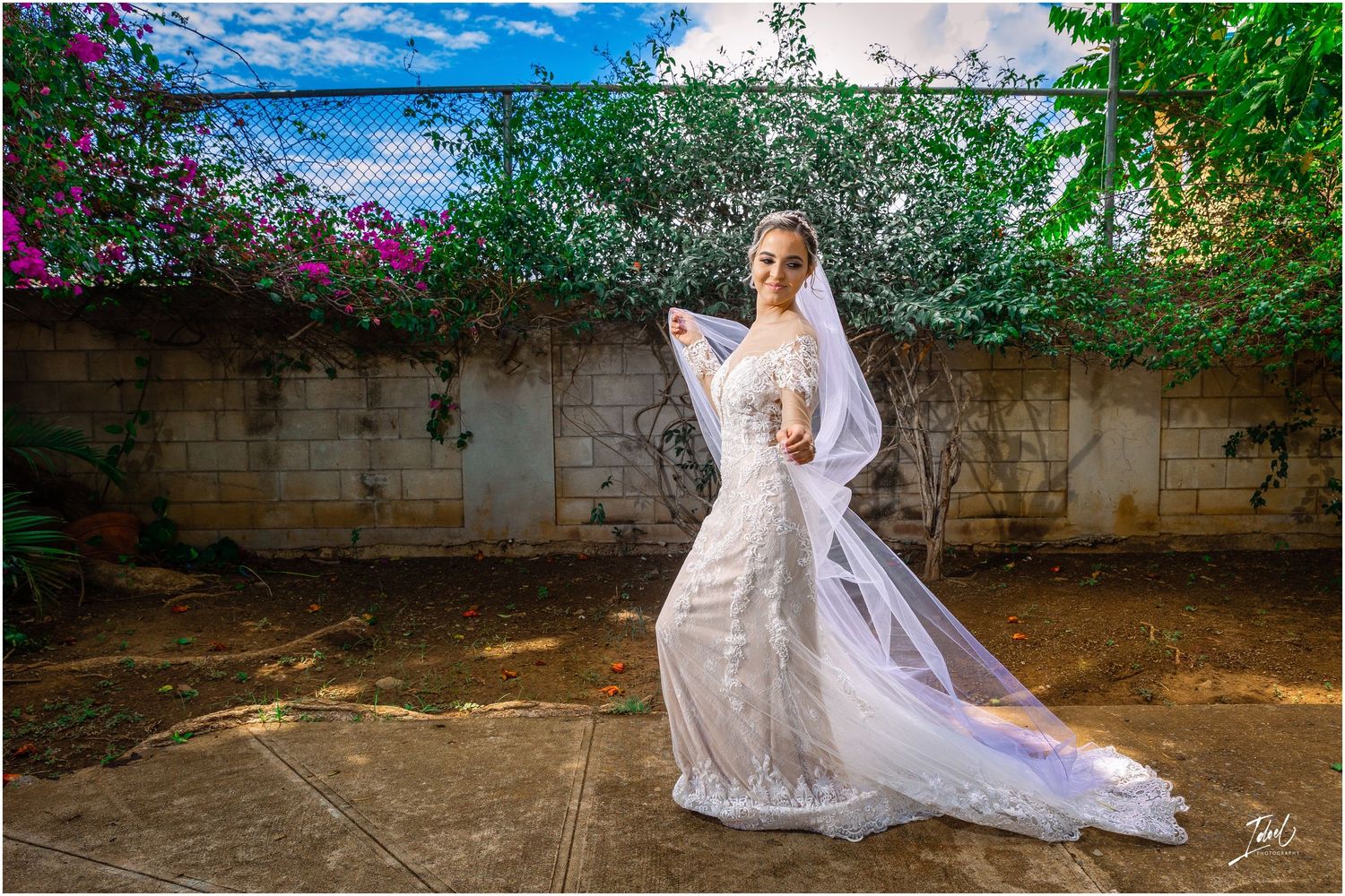 Dramatic bridal portrait in lace gown against stone wall with vibrant purple bougainvillea.