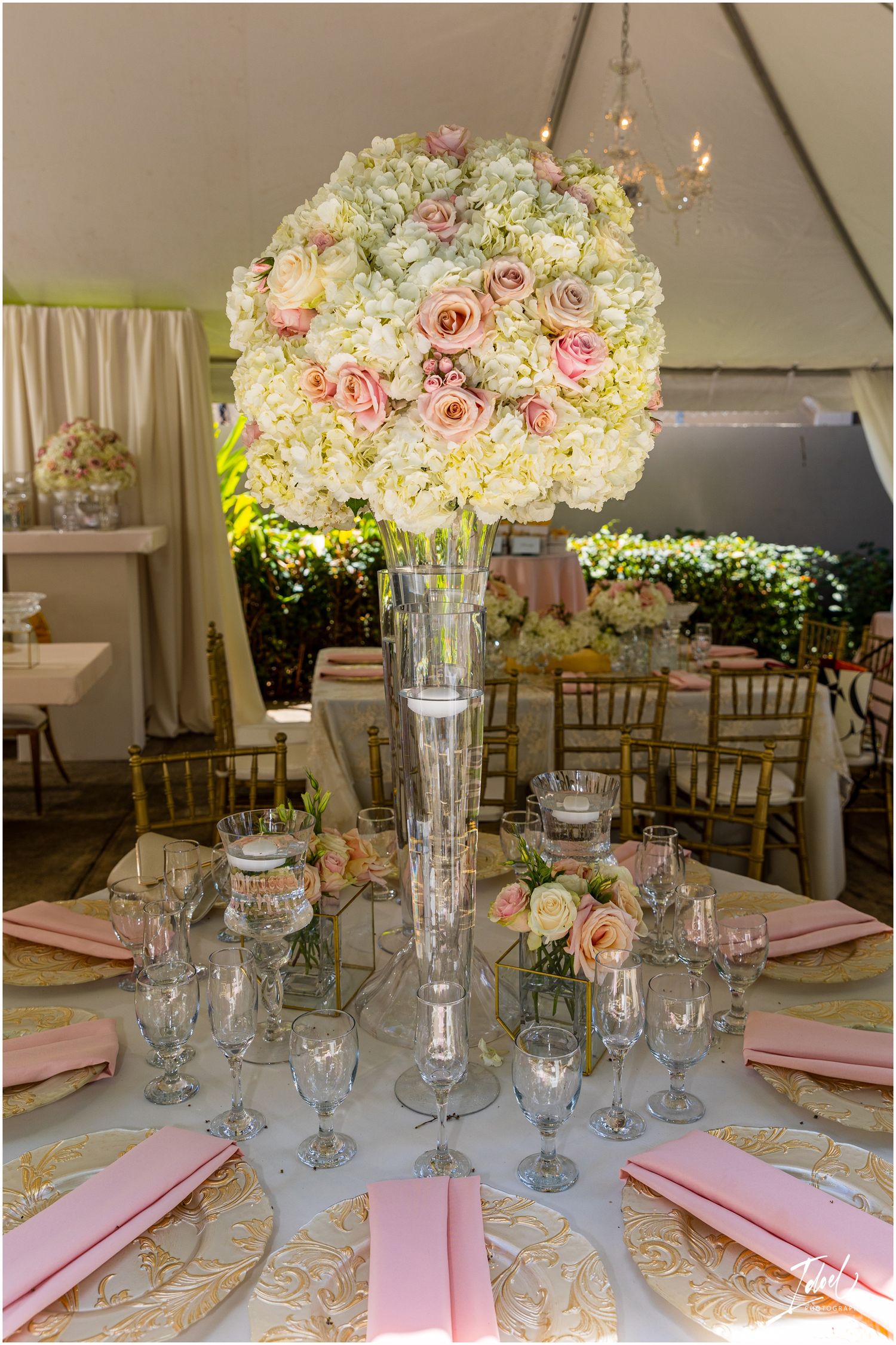 Tall glass centerpiece vase filled with pink and white roses on an elegant table setting.
